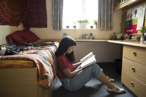 a woman student sitting on the floor in a bedroom reading a book