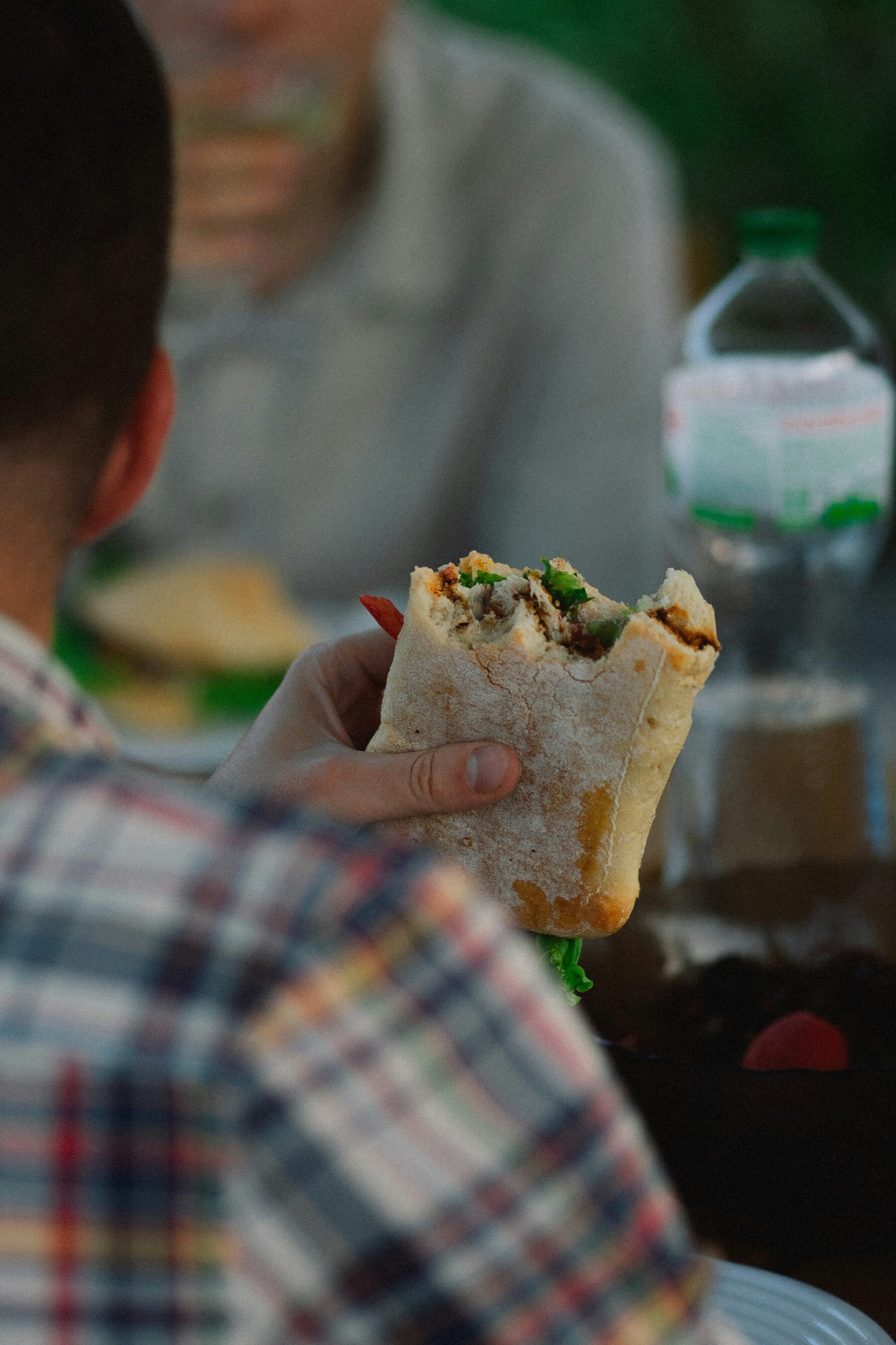 a photo taken from behind, of a man holding a sandwich in his hand that has been partly eaten